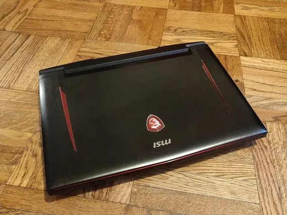 Un portable de jeu MSI noir, fermé, posé sur un parquet, avec des liserés rouges.